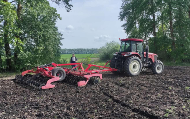  Un tracteur FMWorld est en action, tirant une herse à disques pour le labour.