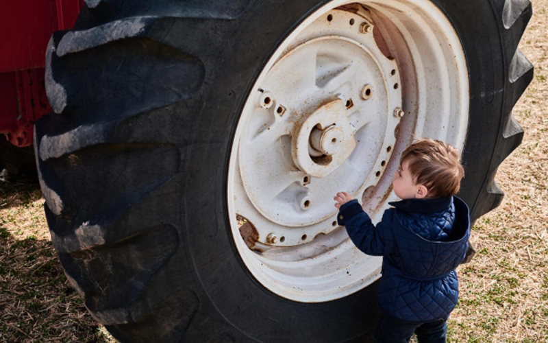 Petit garçon en bleu à côté d'un gros pneu de tracteur, à la recherche de curieux